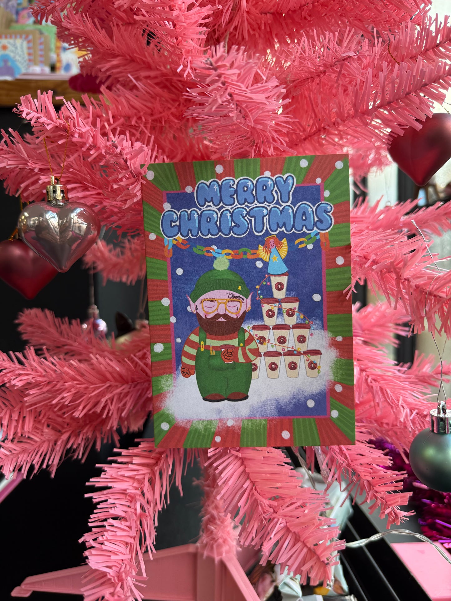 Christmas card with a cartoon character and 'Merry Christmas' text, placed on a pink Christmas tree.
